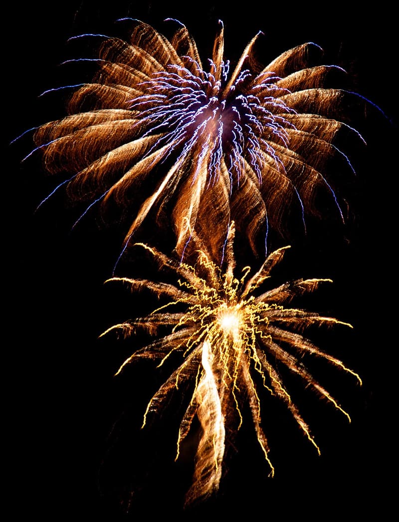 Two colourful aerial fireworks bursting one above the other